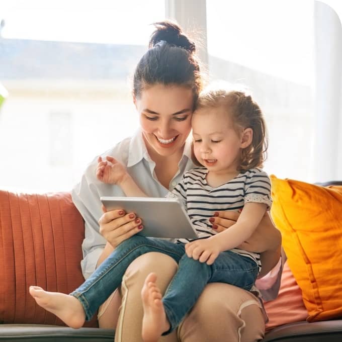 A woman and her daughter look at a tablet while smiling and enjoying Glo Fiber’s lightning-fast in-home Wi-Fi connection.