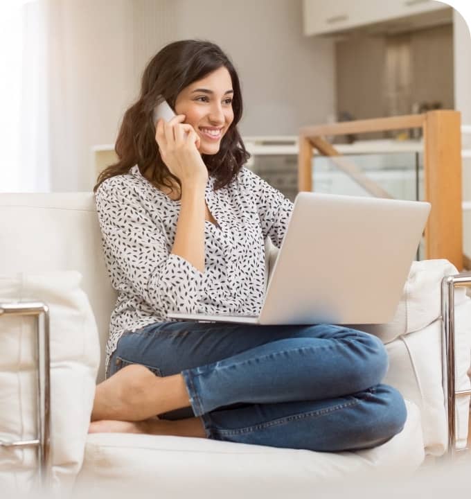 A woman sitting and talking on a phone using fiber Internet home phone service while also using her laptop