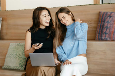 Two woman sitting on a couch laughing at a laptop