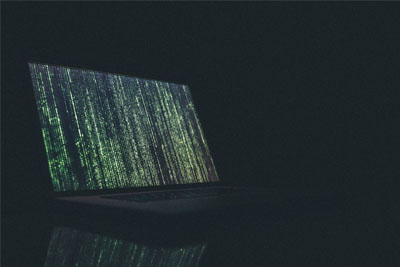 Internet security concept depicting a laptop in a dark room with vertical rows of green text cascading toward the bottom of the screen.