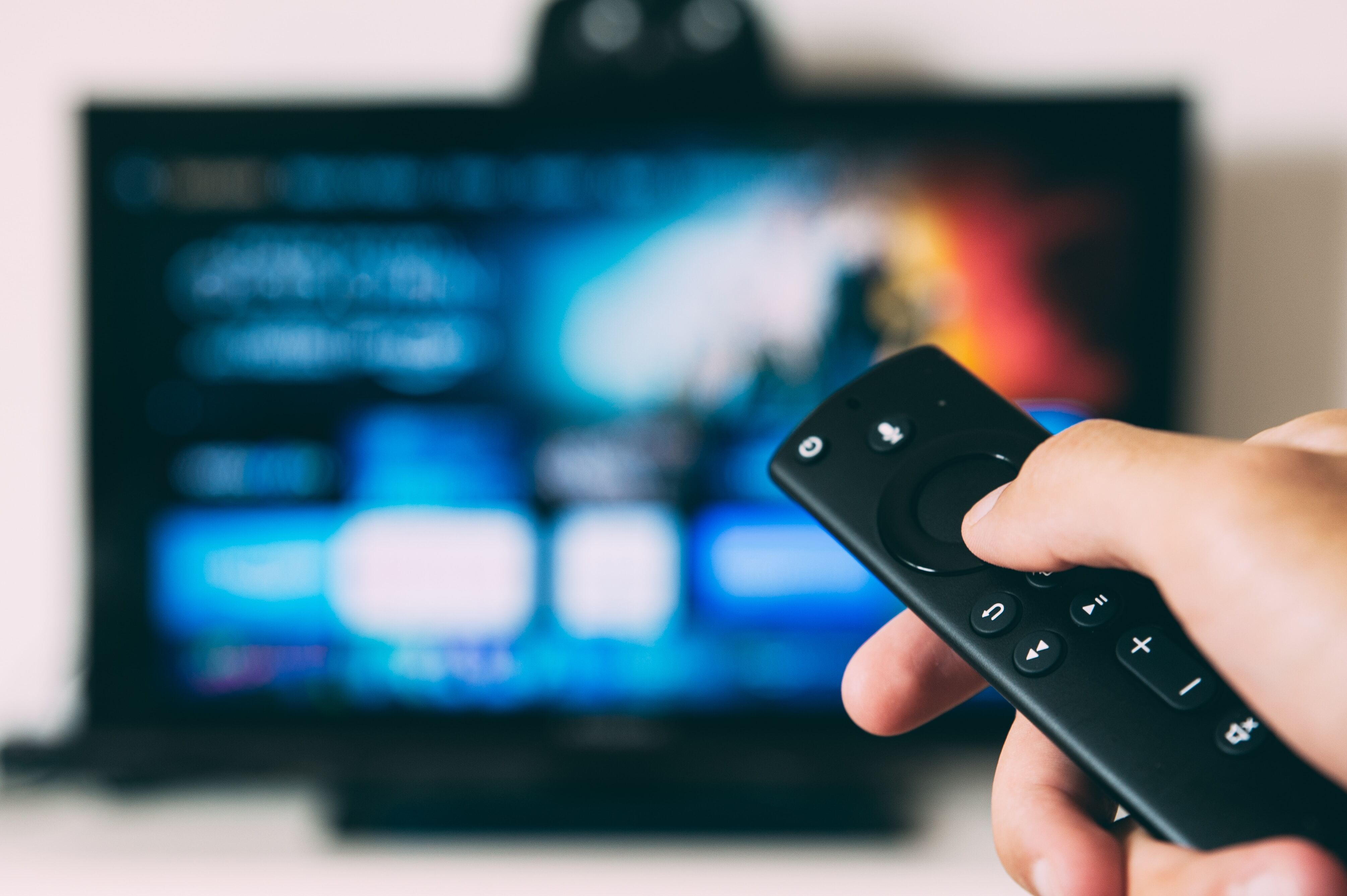 A Glo fiber customer's hand holding a remote and pointing at a blurry tv while streaming a movie using Fiber Internet.