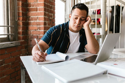 A man writing down notes off his laptop