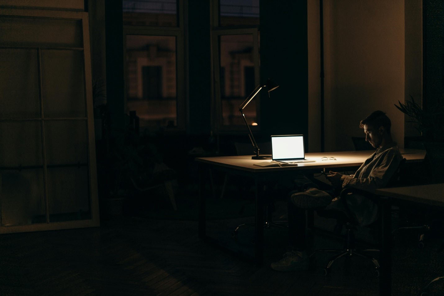 Person sitting at a desk at night using a phone and a laptop