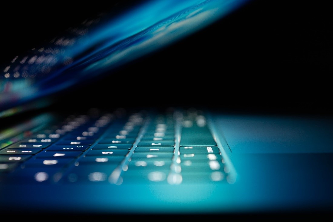 A laptop with its screen nearly folded down and closed. The screen’s backlight shines on the keyboard, illuminating the keyboard.